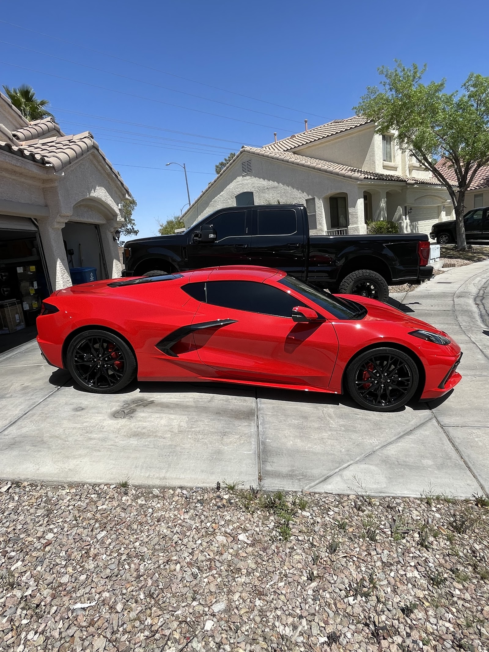 Detailed red Chevrolet Corvette parked in a driveway with a black truck in the background